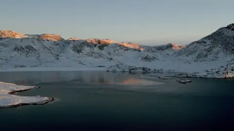 BBC A drone photo of a fjord with snow-capped mountains in the background