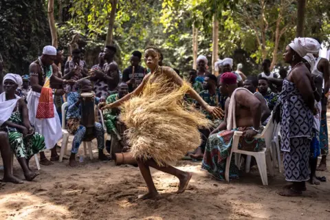 OLYMPIA DE MAISMONT/AFP A voodoo devotee dances during a festival surrounded by people in a forest. 