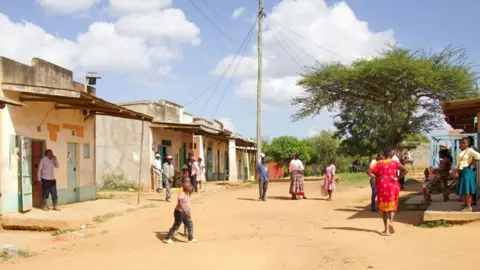 Peter Njorose/BBC The main dirt road through the center of Mukuku village, where a few shops can be seen and residents meet.