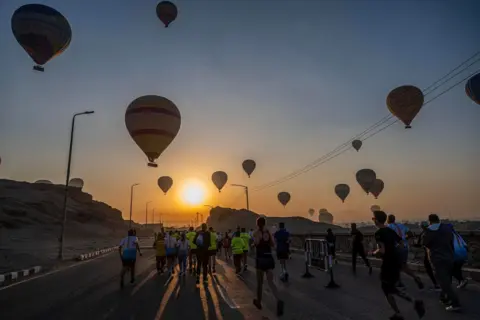 Khaled Desouki / AFP The sun rises over a sky filled with hot air balloons as people run along the streets as part of the Egyptian Marathon.